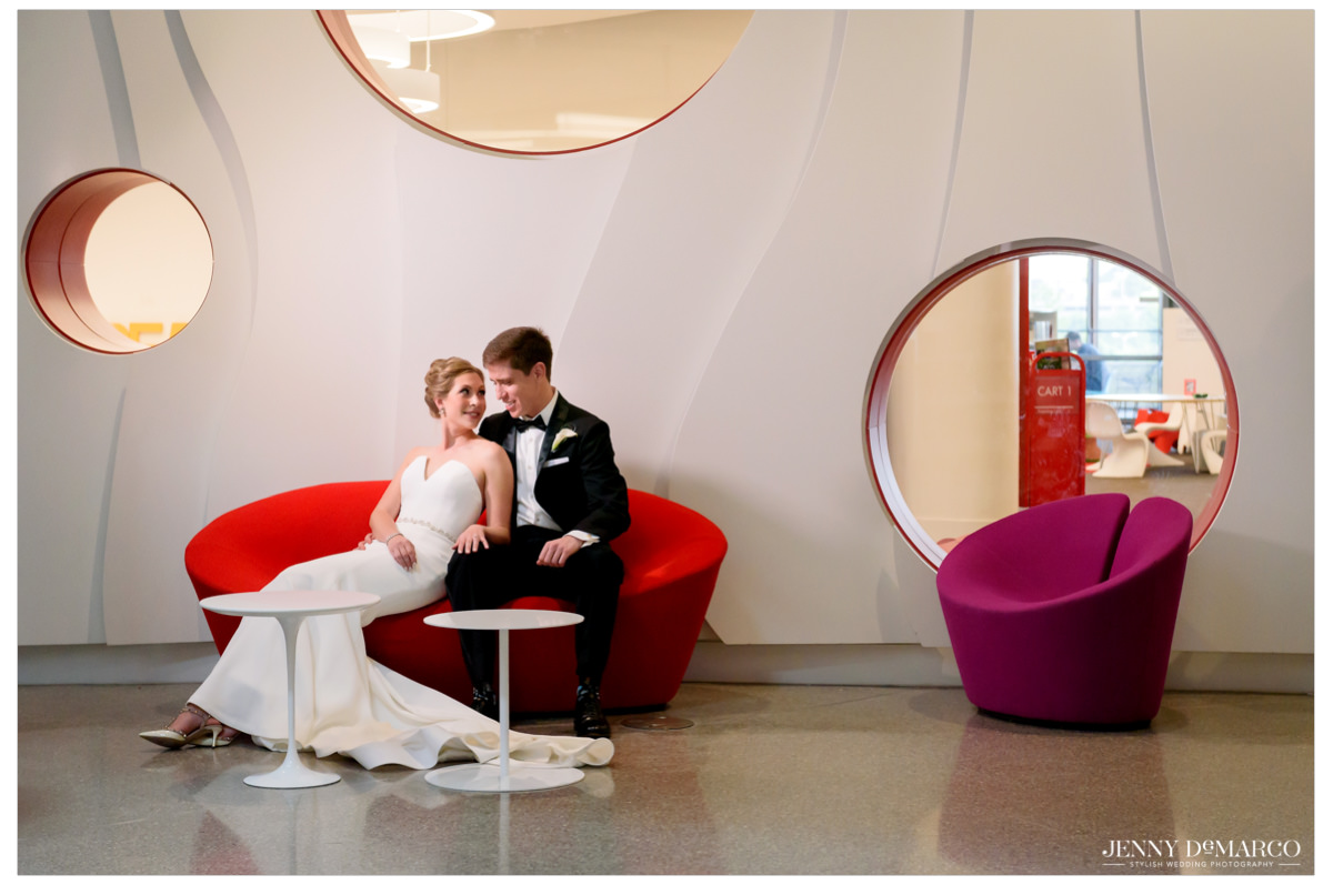 Bride and groom pose on a red couch.